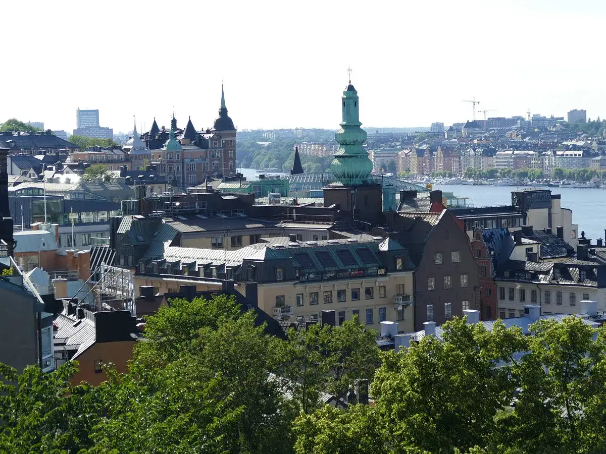 Vy över Stockholms takåsar från Mosebacke terrassen. Grönskande träd i förgrunden.