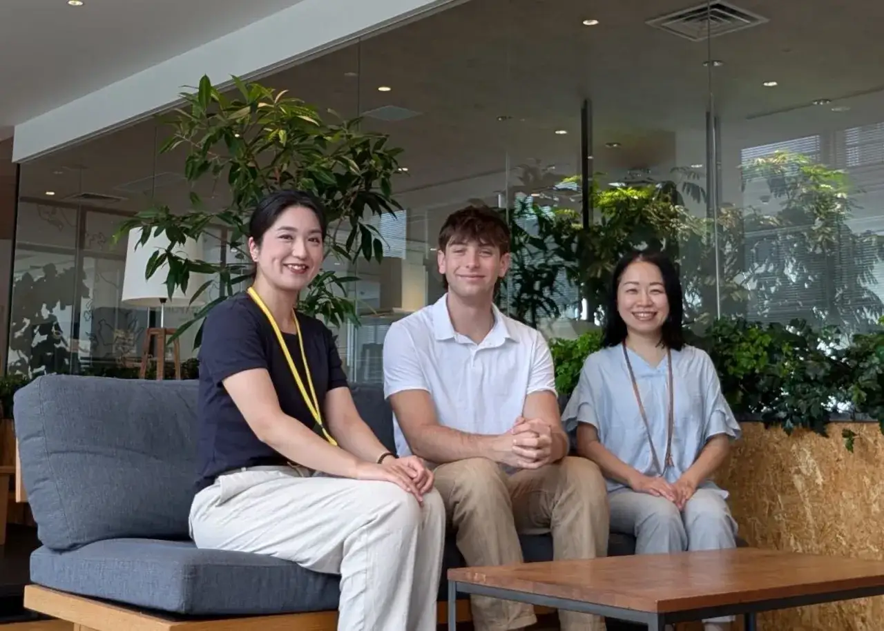 Drei Personen sitzen auf einer Couch. Ein Mann und zwei Frauen l&auml;cheln in die Kamera. Sie sind Teil eines Auslandspraktikums in Japan.
