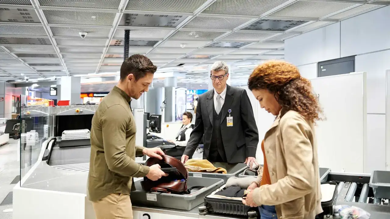 Ein Mann und eine Frau packen Gep&auml;ck f&uuml;r die Sicherheitskontrolle am Flughafen. Gut, dass sie wissen, wie viel eher am Flughafen sein.