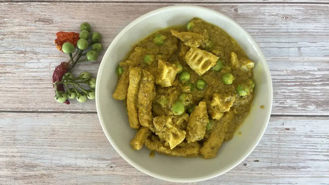 Schüssel mit gelbem, cremigem thai curry ohne kokosmilch, Erbsen und Lotuswurzel. Daneben ein Zweig mit grünen Beeren und getrockneten Chilis.