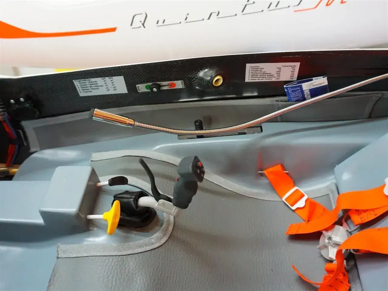 Cockpit-Ansicht mit Steuerknüppel, Gurten und einer kleinen Pilotenpuppe 1/3. Ein Aufkleber zeigt Flugzustände und eine Checkliste.