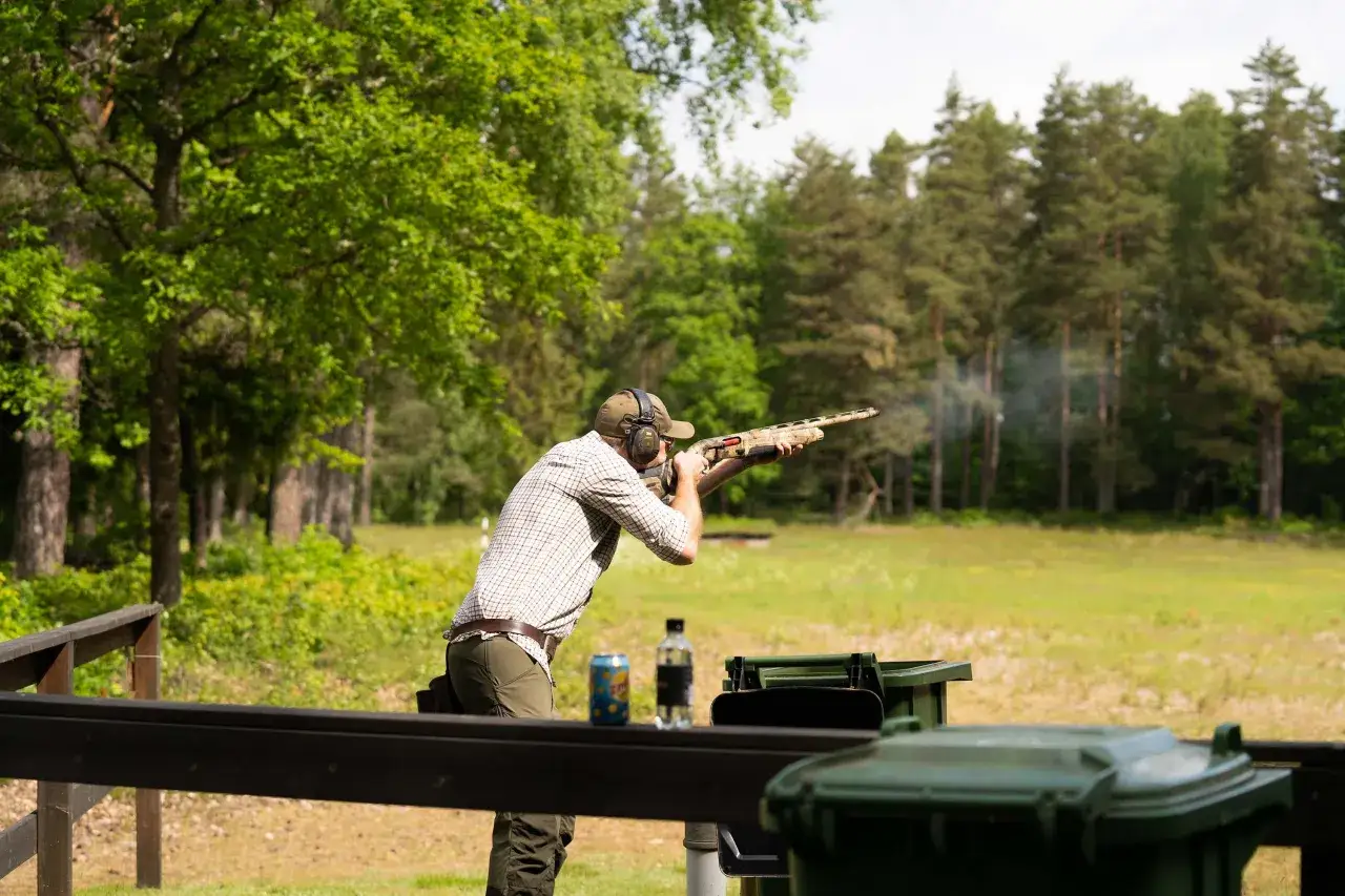 Man i hörselskydd skjuter hagelgevär i form av lerduveskytte. Rök stiger från vapnet.