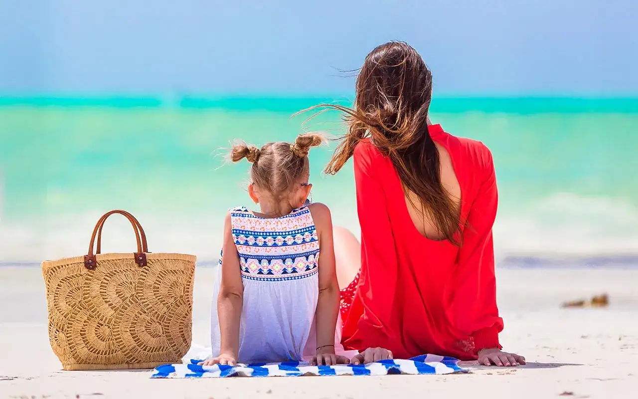 Mama i córka na plaży, obok koszyk plażowy. Idealny zestaw, by wiedzieć, co zabrać na wakacje nad morze z dzieckiem.