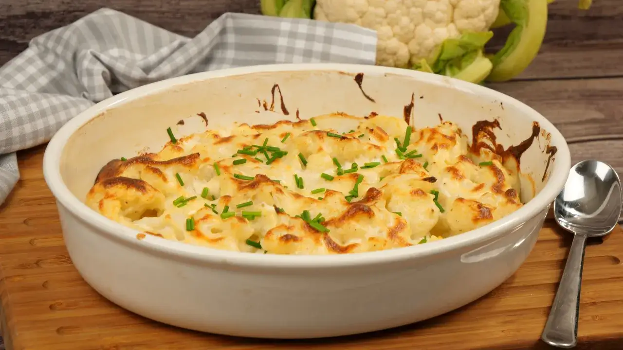 Ein goldbraun überbackener Blumenkohlauflauf mit cremiger Käsesauce und frischen Kräutern garniert.