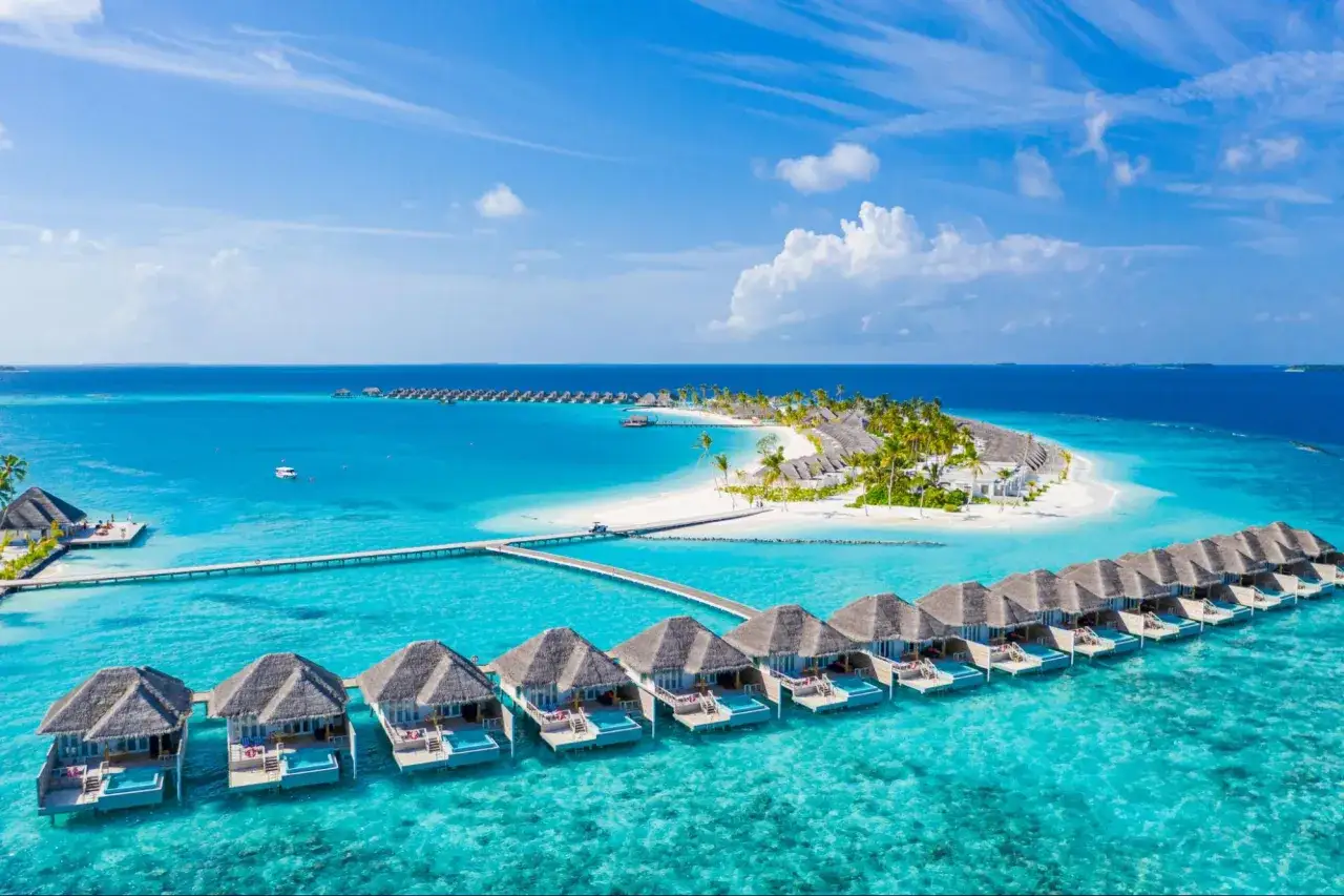 Bungalows sobre el agua en un resort de Maldivas, con aguas turquesas y una isla tropical. ¡Un sueño de Maldivas low cost!