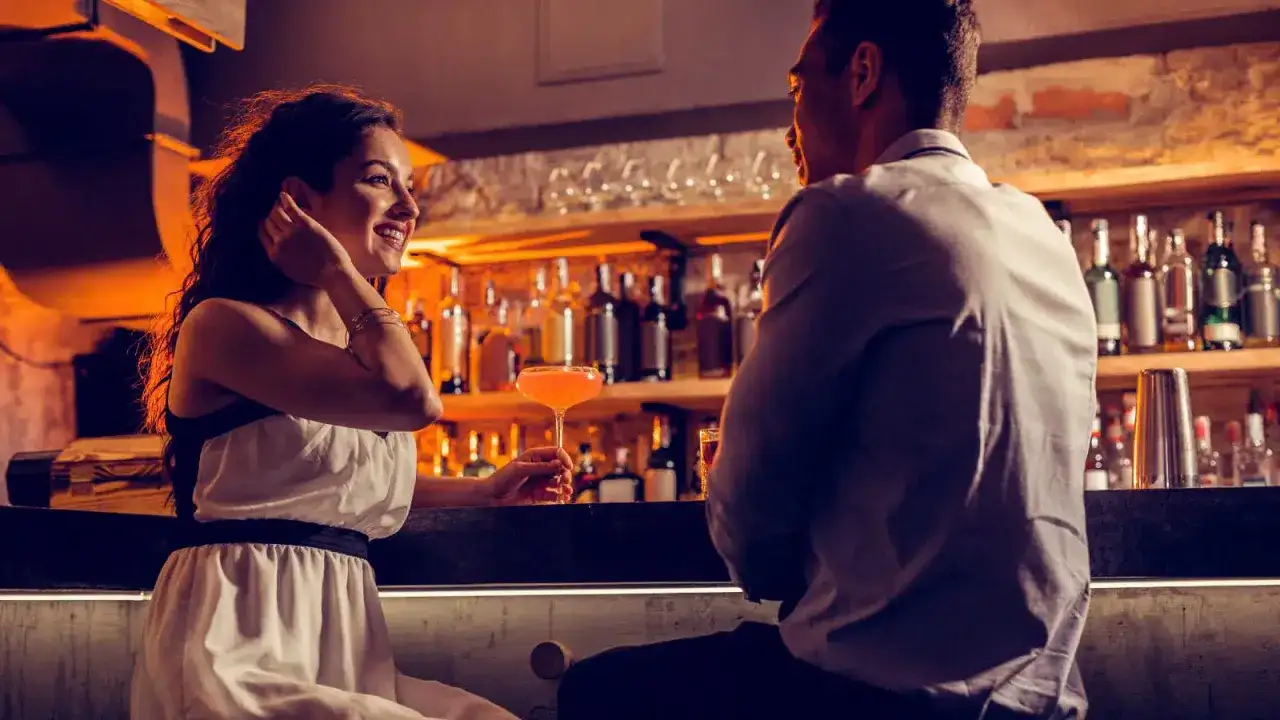 Coppia al bancone di un bar, lei sorride, lui la guarda. Un drink in mano, un momento di corteggiamento: quando mollare?