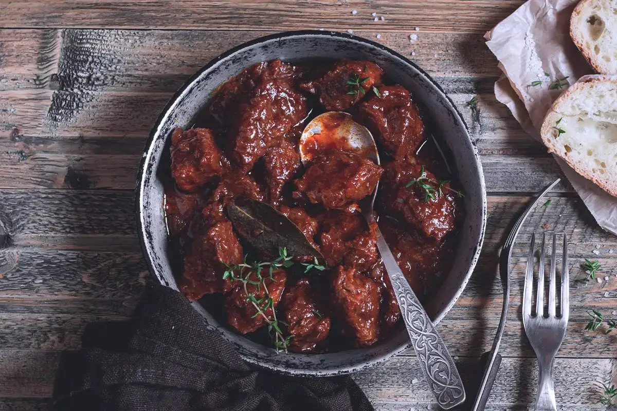 Un invitante piatto di stracotto di manzo, cotto lentamente in una ricca salsa scura, guarnito con erbe aromatiche fresche.