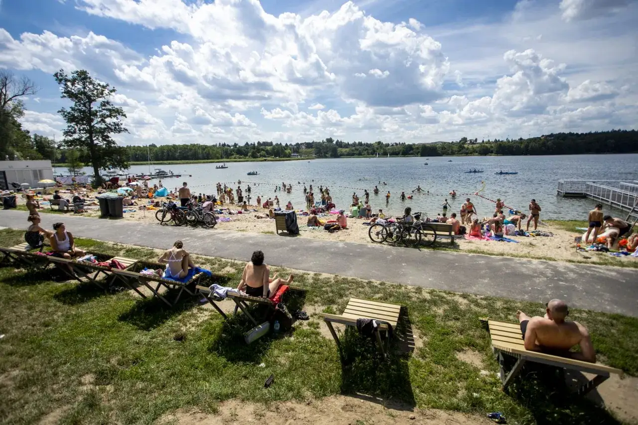 Tłum ludzi odpoczywa nad jeziorem w Kiekżu. Kąpielisko tętni życiem, a na plaży widać wiele rowerów.