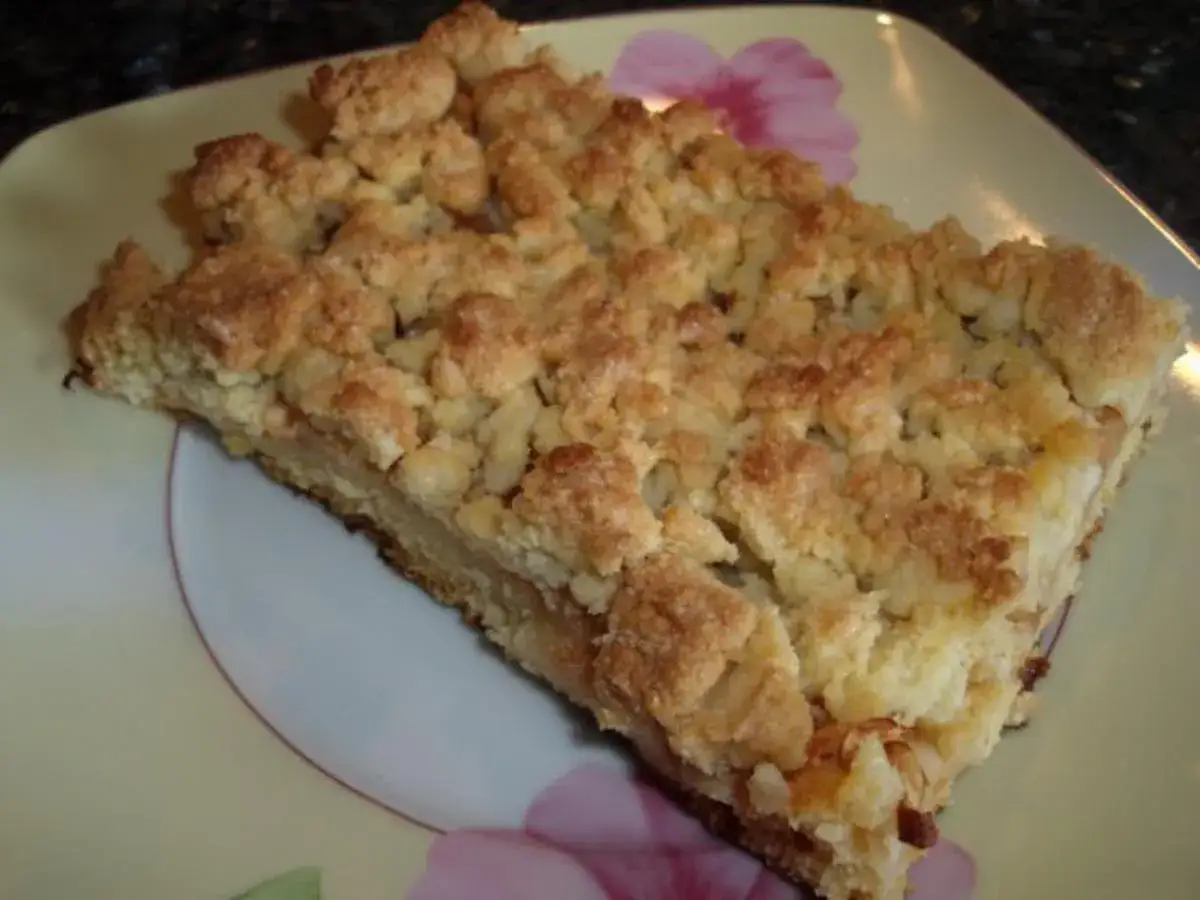 Ein St&uuml;ck saftiger Apfelkuchen vom Blech mit knuspriger Streuseldecke auf einem Teller mit Blumenmuster.