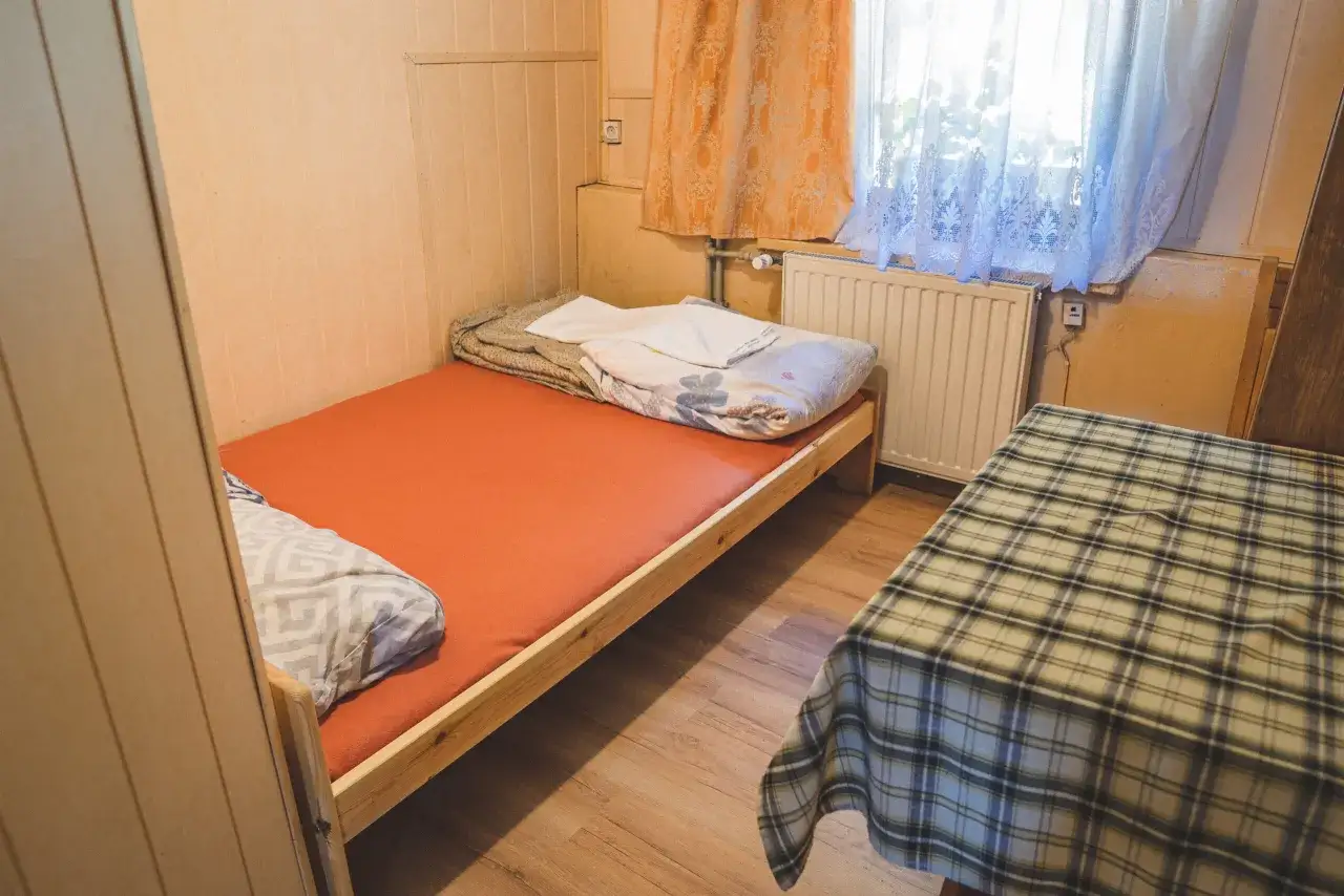 Proste łóżko i stolik w kratę. Różnica między schroniskiem PTTK a prywatną bazą noclegową bywa widoczna w takich szczegółach.