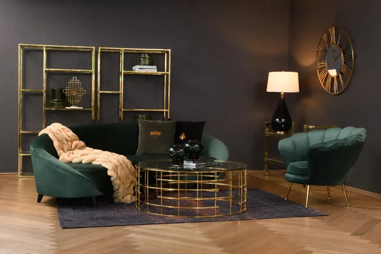 Butelkowa zieleń z czym łączyć wnętrza? Elegancka sofa i fotel w tym kolorze, złote dodatki i ciepły pled tworzą przytulną aranżację.