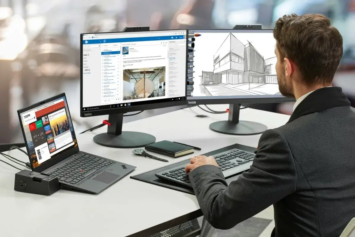 Mann am Schreibtisch mit zwei Monitoren und Laptop. Die Lenovo Tastatur geht nicht, er versucht es mit einer externen.