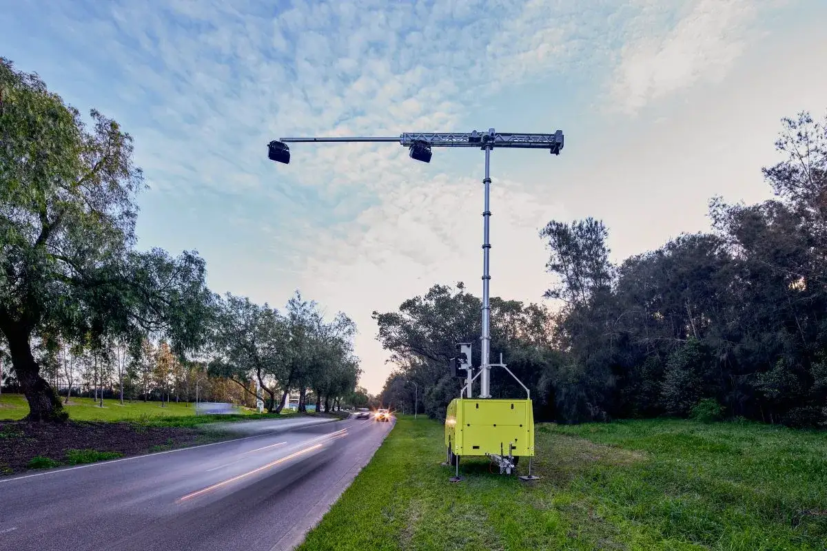 Un radar ceinture mobile surveille la circulation sur une route bord&eacute;e d'arbres. Le ciel est nuageux.