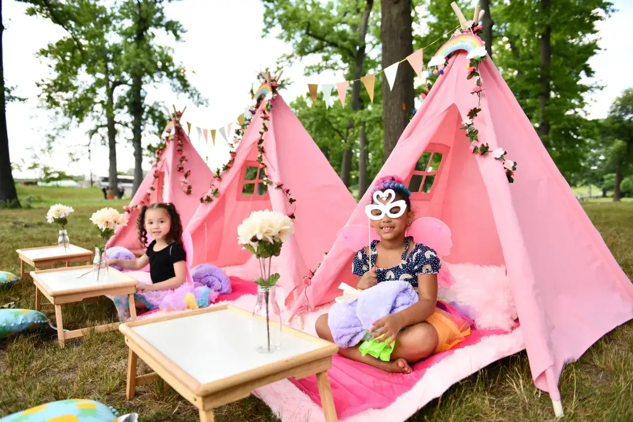 Różowe namioty tipi z dekoracjami to wspaniałe atrakcje na urodziny dziecka w ogrodzie. Dwie dziewczynki cieszą się magiczną atmosferą.