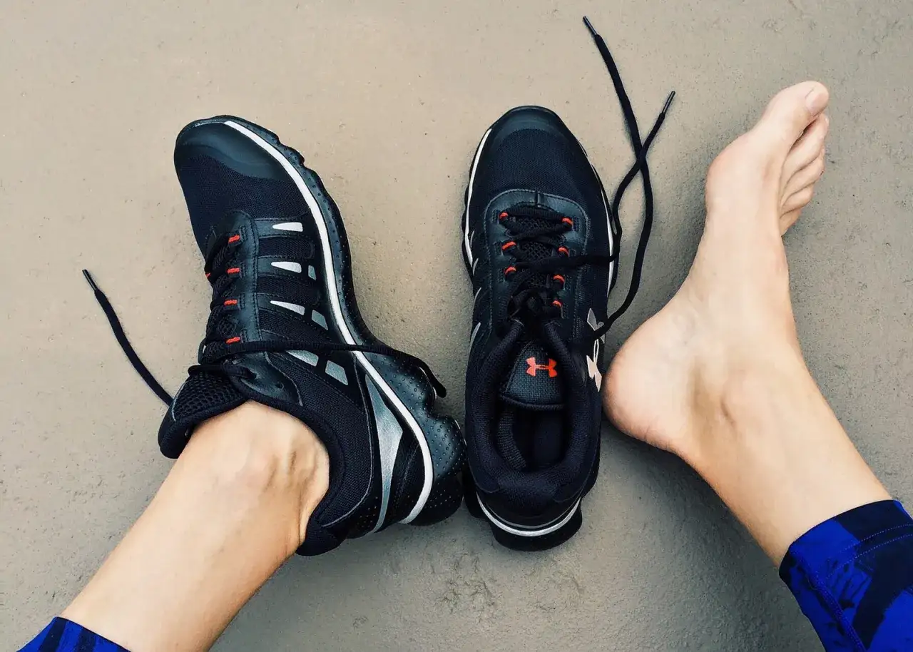 Schwarze Laufschuhe mit roten Akzenten, bereit zum Einlaufen. Ein Fu&szlig; ist bereits im Schuh, der andere liegt daneben.
