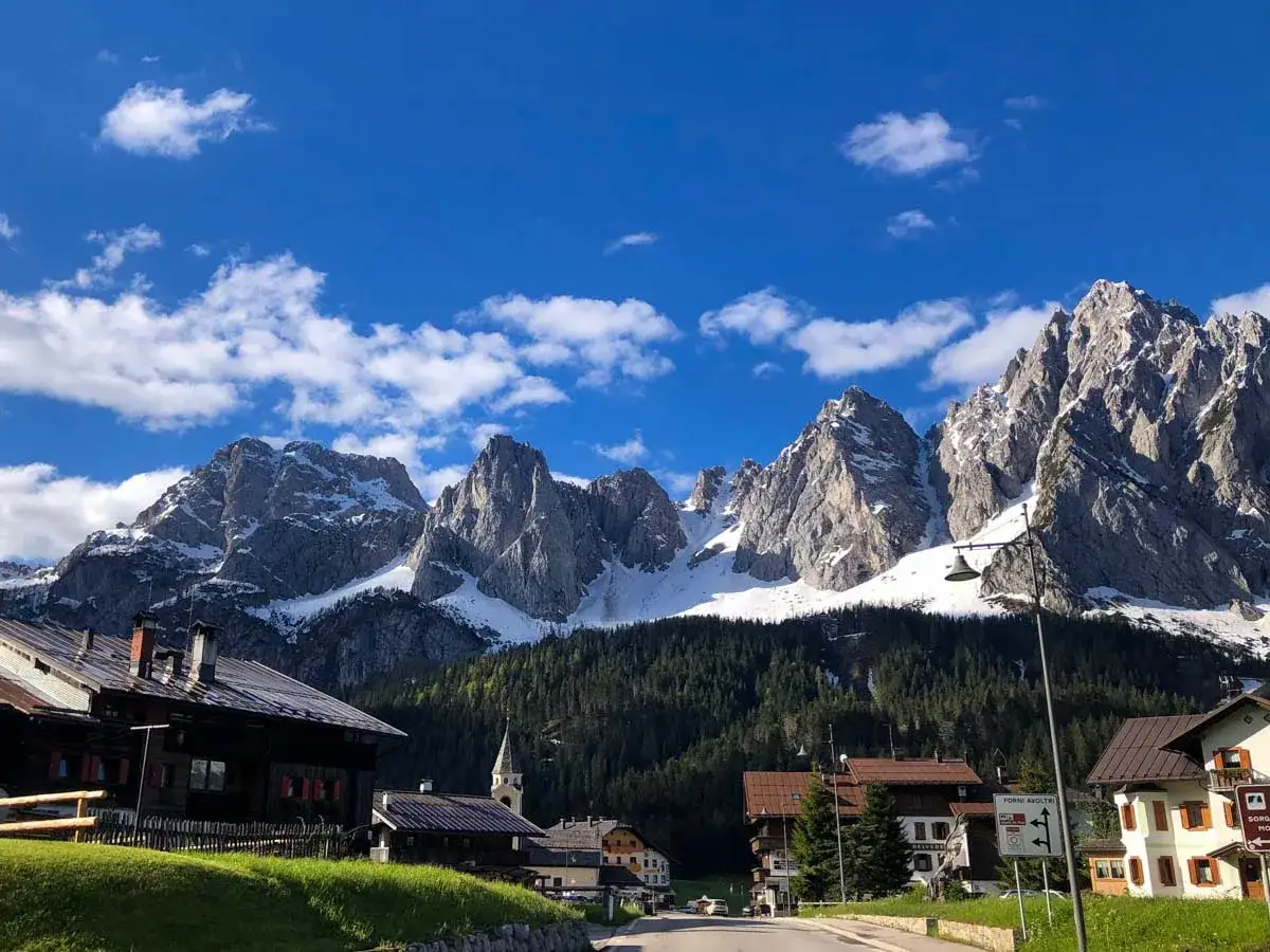 Un incantevole carnia paese con case in legno e tetti spioventi, incorniciato da maestose montagne innevate sotto un cielo azzurro.