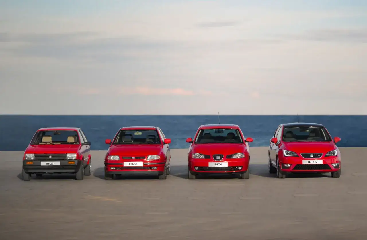 Cuatro generaciones de seat ibiza modelos, alineados frente al mar, mostrando la evoluci&oacute;n del dise&ntilde;o automotriz.