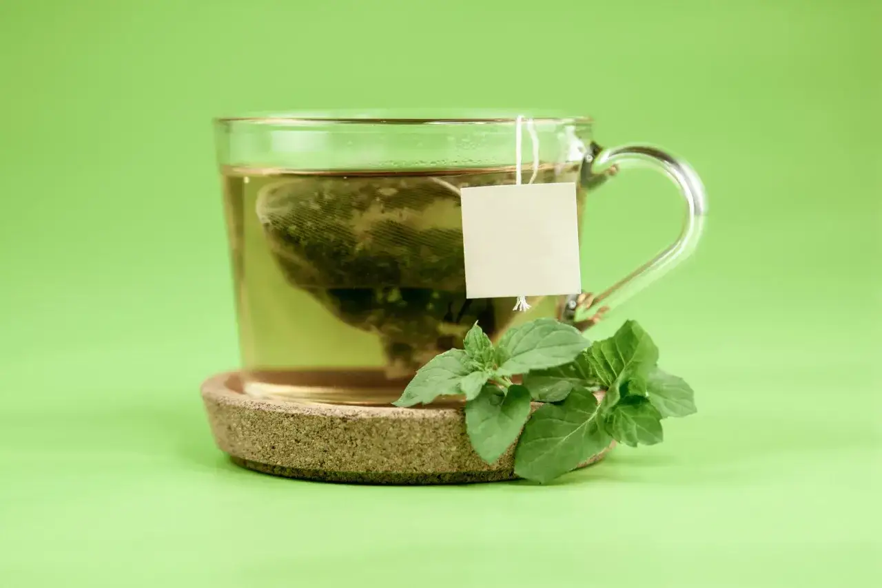 Une tasse de thé vert, avec des feuilles de menthe fraîche. Le thé vert est connu pour ses vertus, mais il faut aussi connaître ses méfaits.