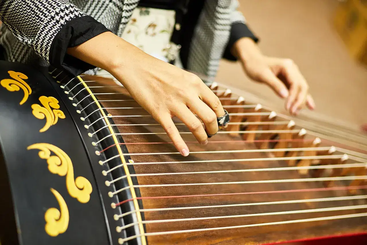 Mains jouant un guzheng, un instrument de musique d'Asie, orn&eacute; de motifs dor&eacute;s.