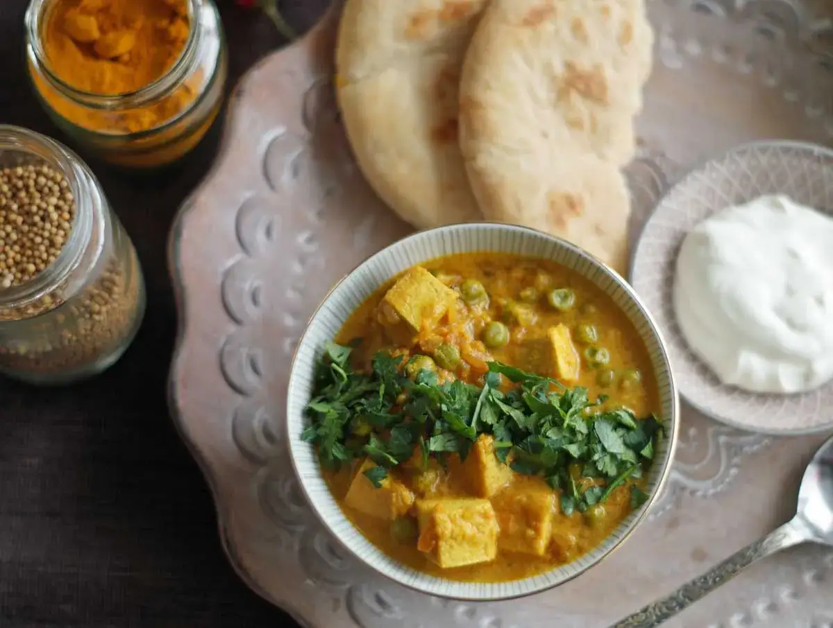 Sch&uuml;ssel mit cremigem Mattar Paneer, garniert mit Koriander. Daneben Naan, Joghurt und Gew&uuml;rze.