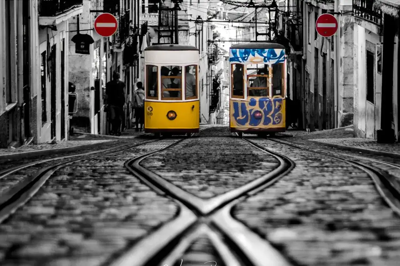 Deux tramways emblématiques de Lisbonne, l'un jaune vif, l'autre tagué, sur des rails pavés. Une scène typique pour savoir que faire à Lisbonne.