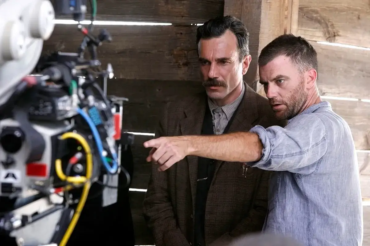 Regiss&ouml;ren Paul Thomas Anderson pekar mot kameran medan Daniel Day-Lewis lyssnar uppm&auml;rksamt. En scen fr&aring;n inspelningen av filmer med Paul Thomas Anderson.