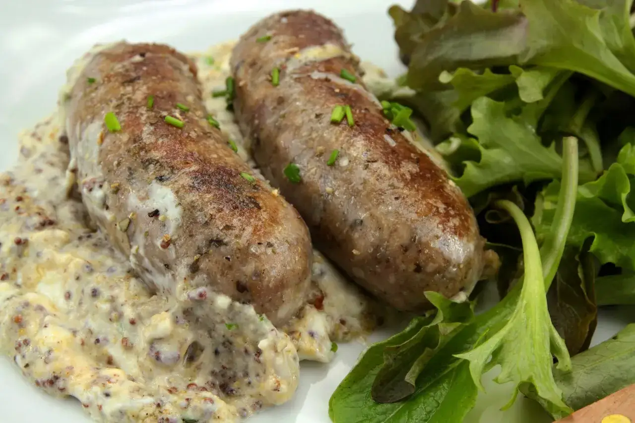 Deux andouillettes artisanales savoureuses, nappées d'une sauce à la moutarde et accompagnées d'une salade verte croquante.