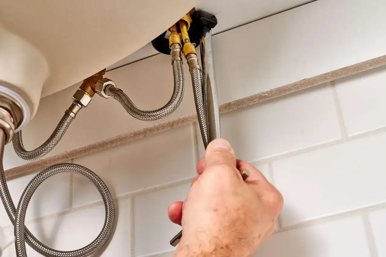 A hand uses a wrench to disconnect the water supply lines, a key step in how to remove a kitchen faucet.