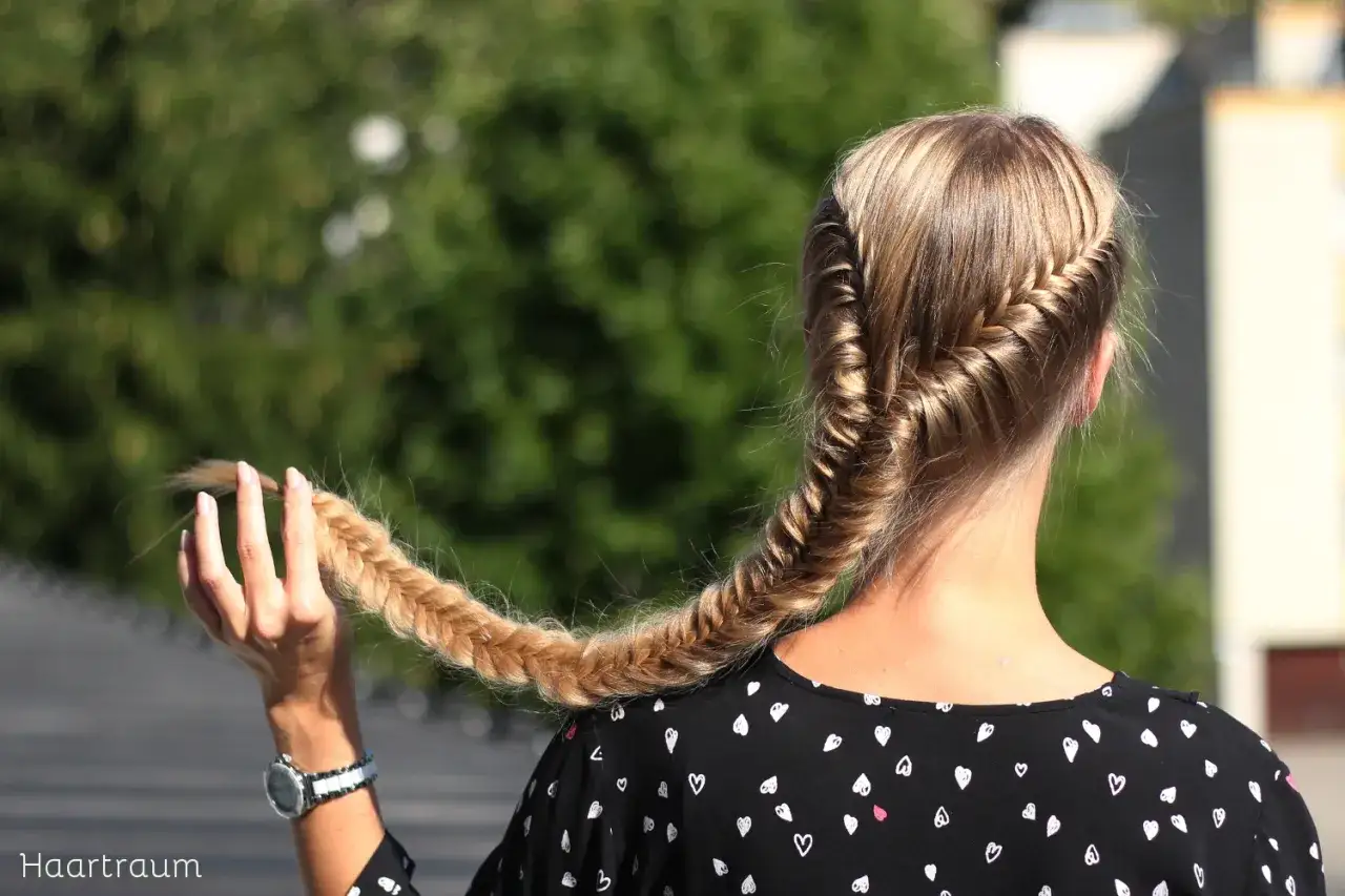 Ein Fischgrätenzopf, der zeigt, wie **haare zu lang** werden können. Die Hand hält die Spitze des geflochtenen Zopfes.