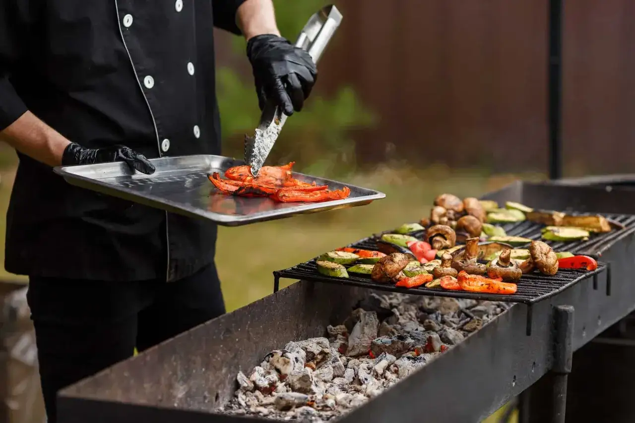 Szef kuchni dodaje pieczoną paprykę do grillowanych warzyw. Aromatyczne jedzenie na grilla kusi z rusztu.