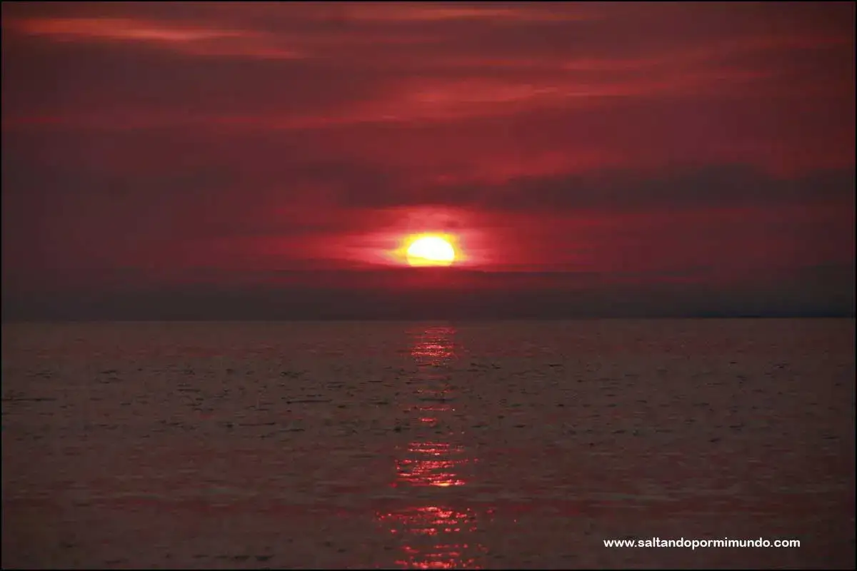 Atardecer carmesí sobre el mar, con el sol asomando en el horizonte, reflejándose en las aguas. Una vista espectacular desde la punta faxilda.
