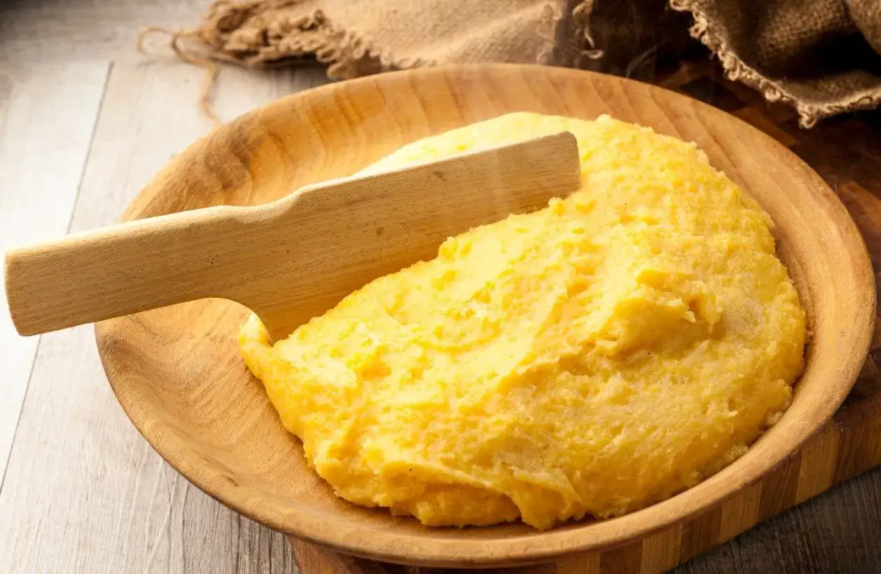 Gorąca polenta, czyli co to jest? Żółta, kremowa kaszka kukurydziana podana w drewnianej misce, z drewnianą łopatką.