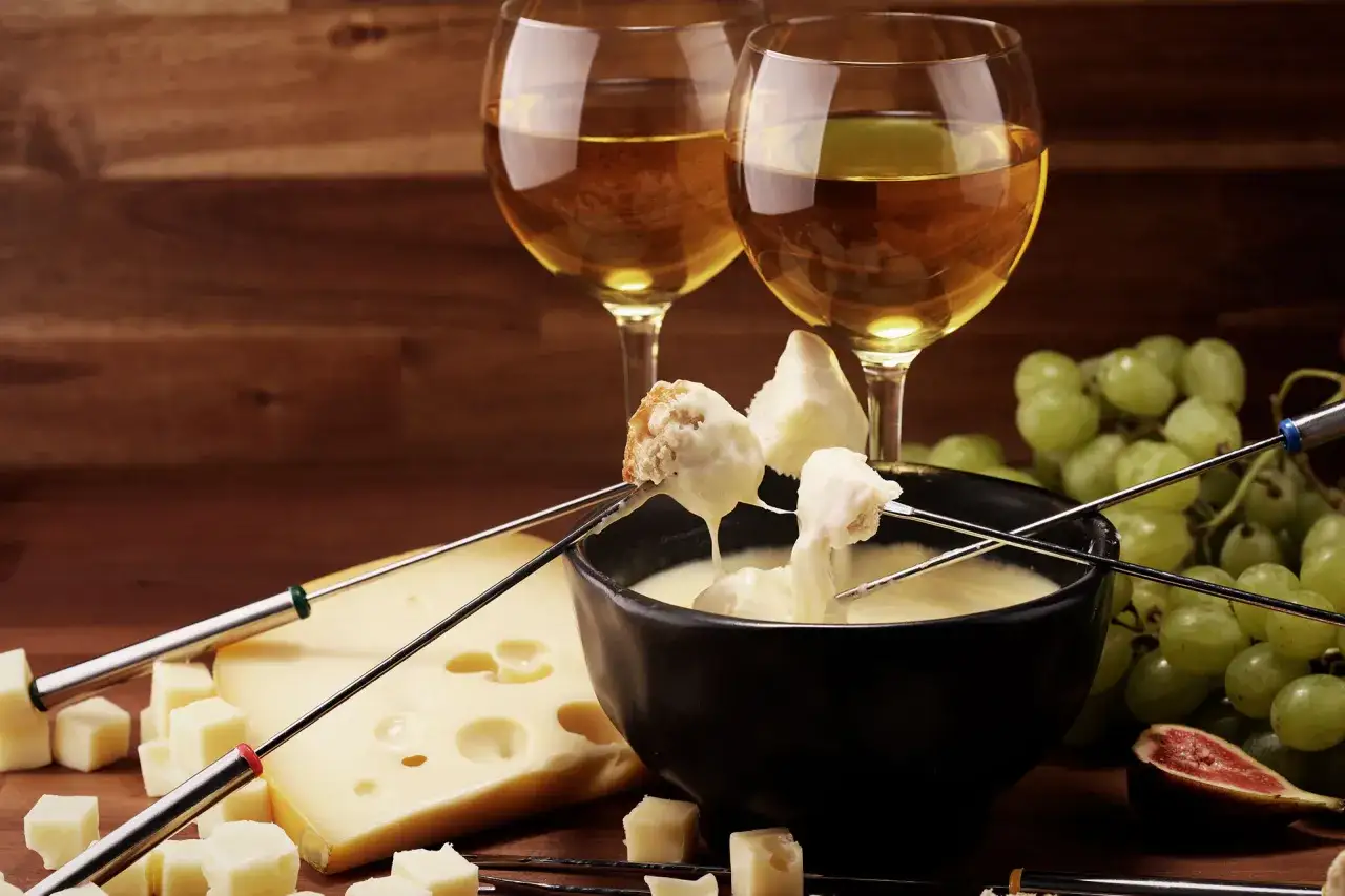 Una deliziosa fonduta di formaggio con pane e uva, accompagnata da due calici di vino bianco.