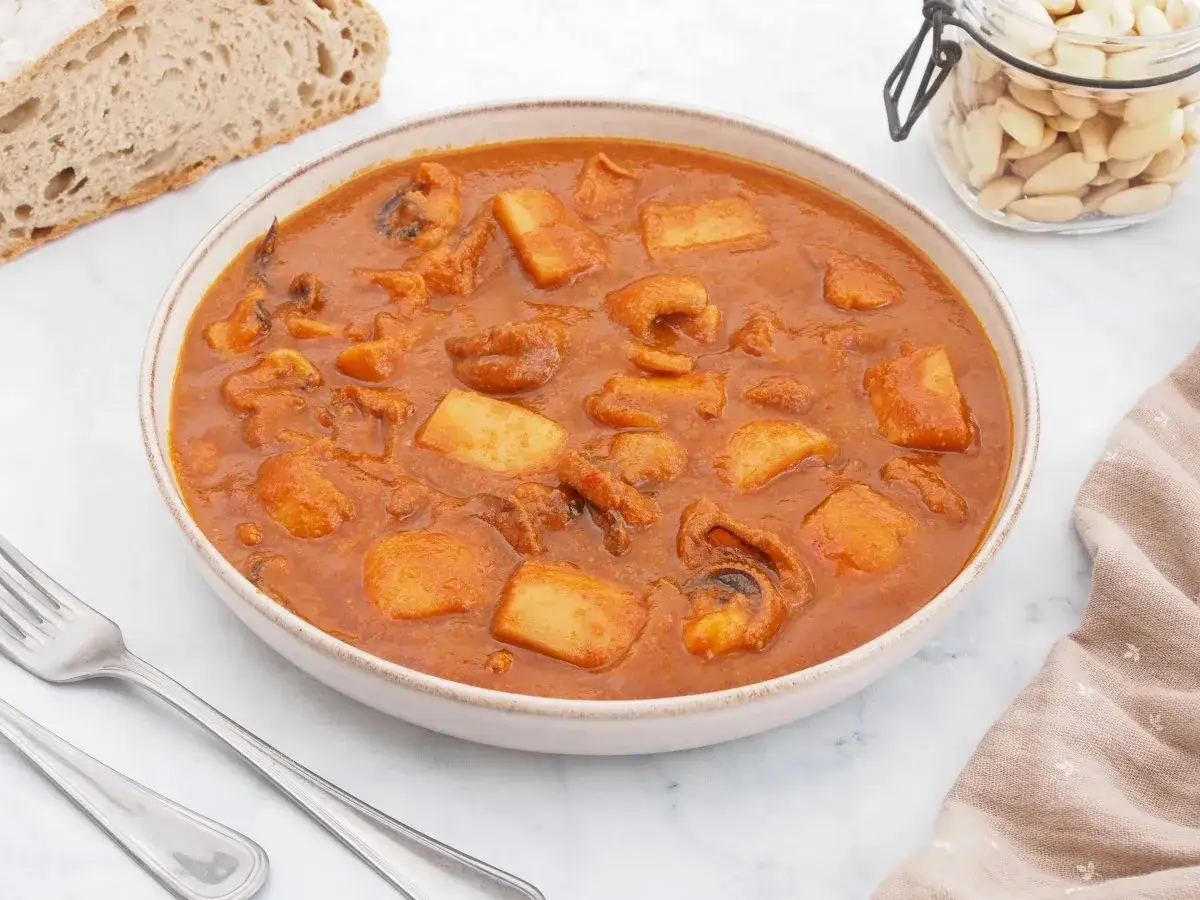 Un plato humeante de jibia en salsa, con trozos de patata y pan rústico al lado.