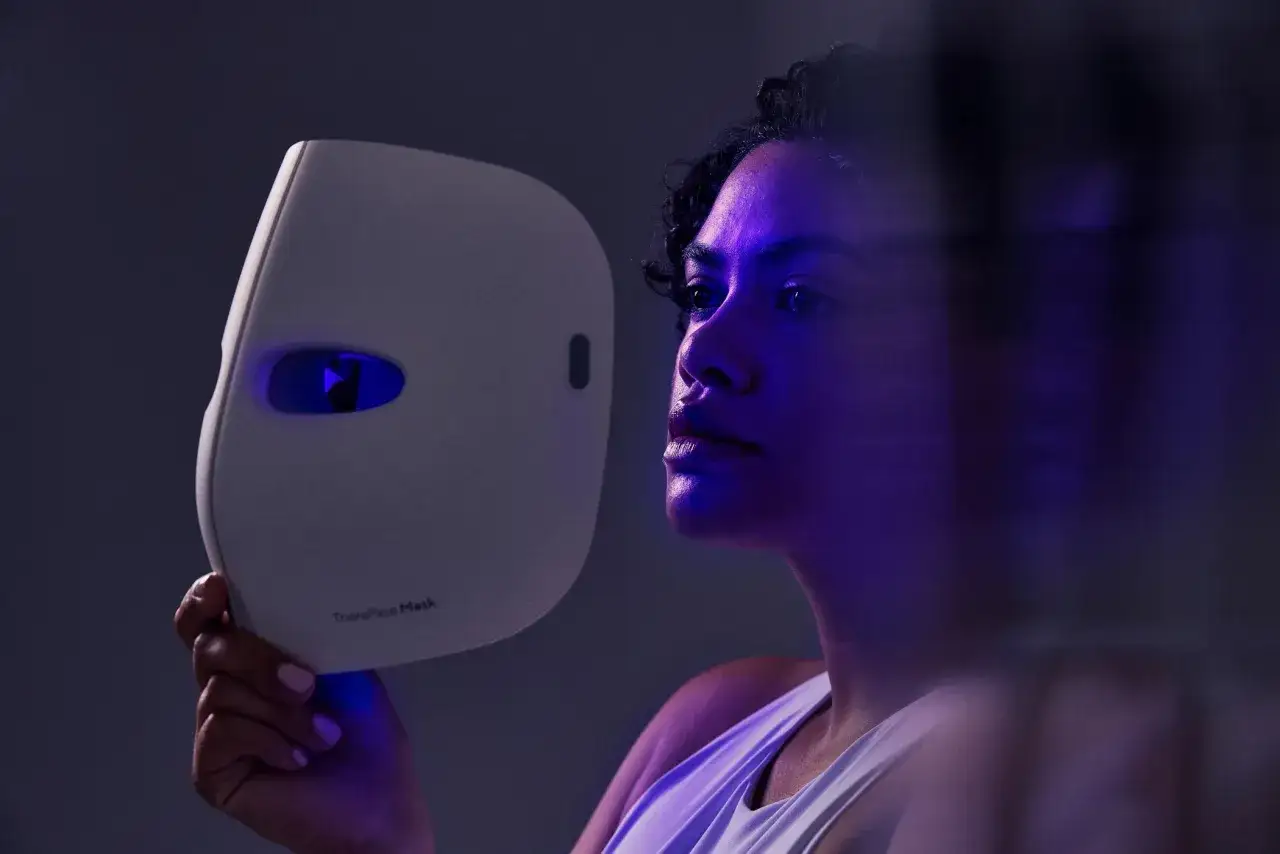A woman holds a white mask emitting blue light, showcasing the blue light benefits for skin.