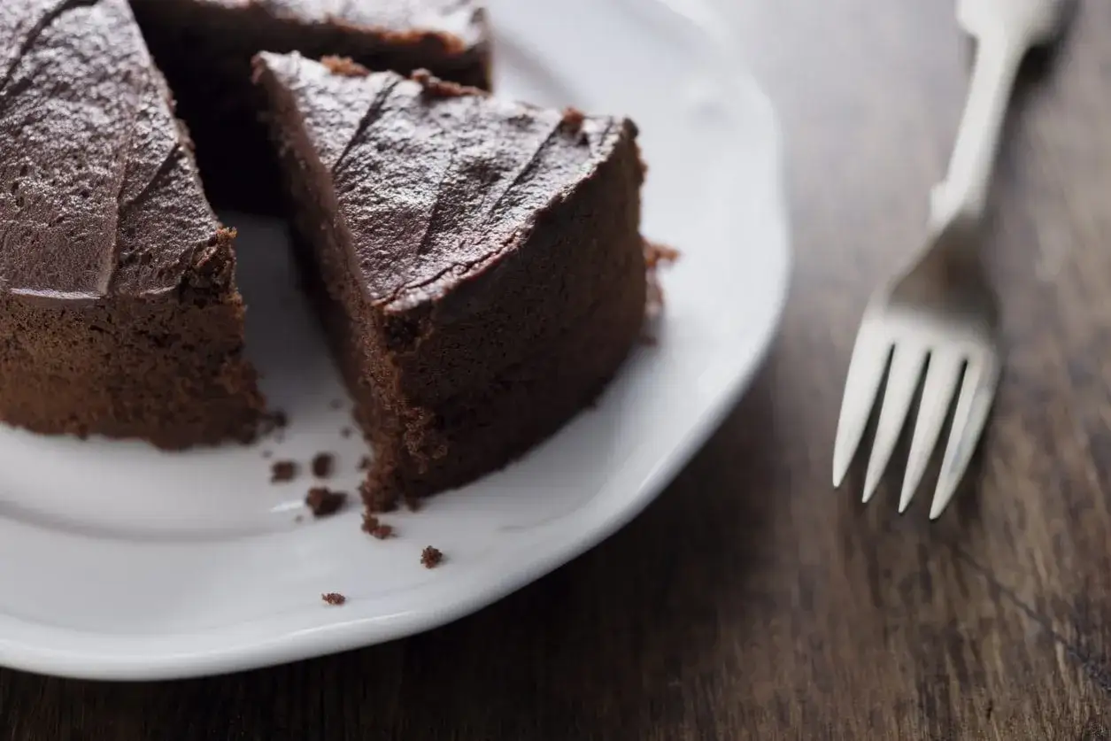 Una fetta di torta al cioccolato scuro, umida e invitante, su un piatto bianco. Perfetta per chi cerca dolci senza zucchero.
