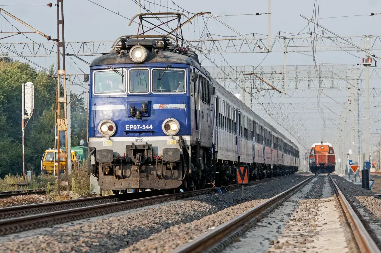 Niebieska lokomotywa z pantografem EP07-544 PKP Intercity zbliża się do widza, obok niej widać inny pociąg.