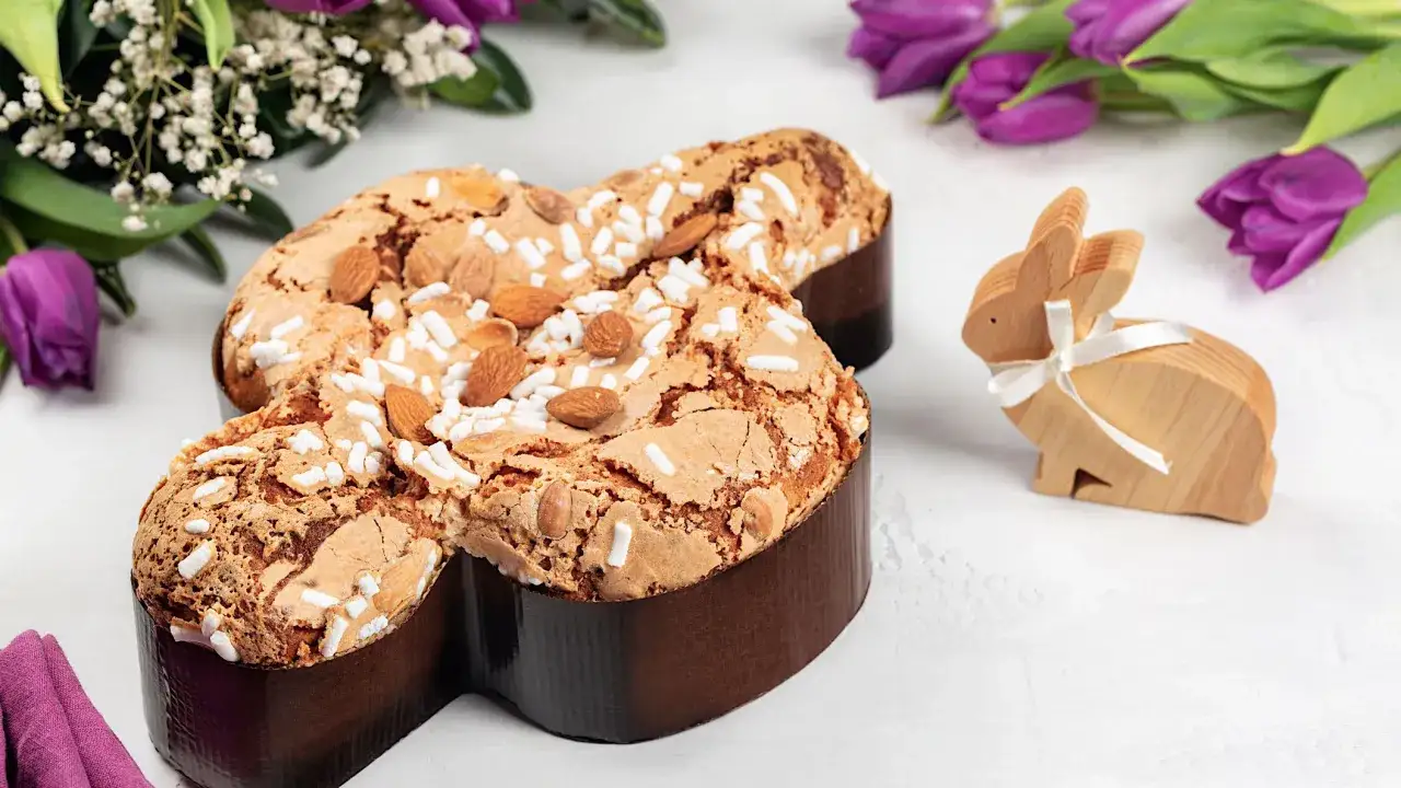 La colomba, un dulce tradicional de Pascua, adornada con almendras y azúcar, junto a un conejito de madera y tulipanes morados.