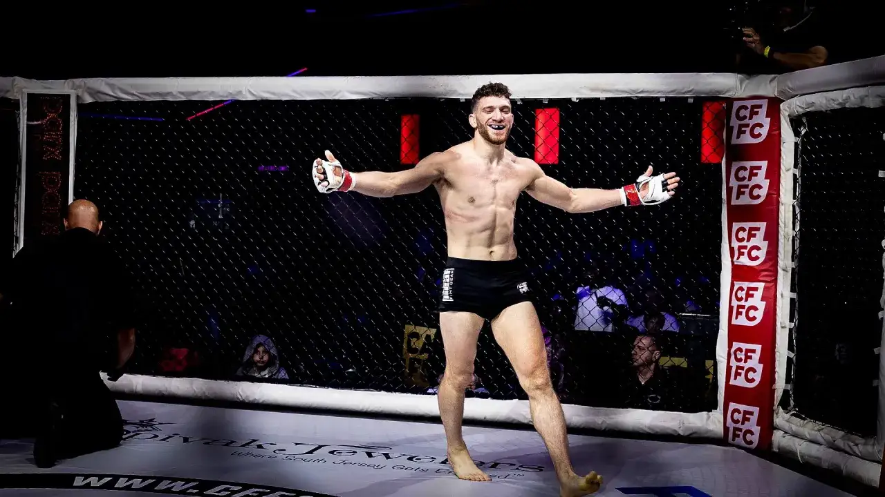 En glad MMA-fighter med armarna utstr&auml;ckta i buren, redo f&ouml;r det b&auml;sta av MMA.