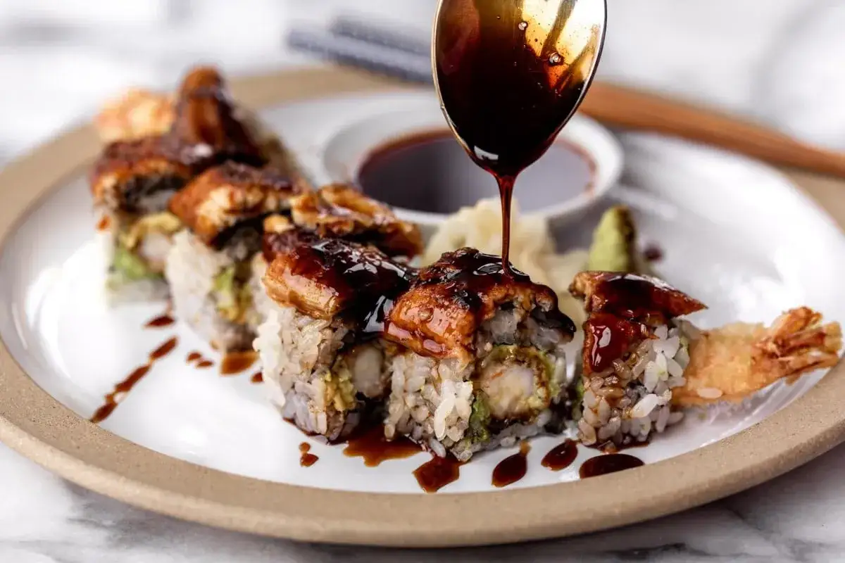 Roladki sushi z krewetką w tempurze i awokado, polane błyszczącym sosem unagi.