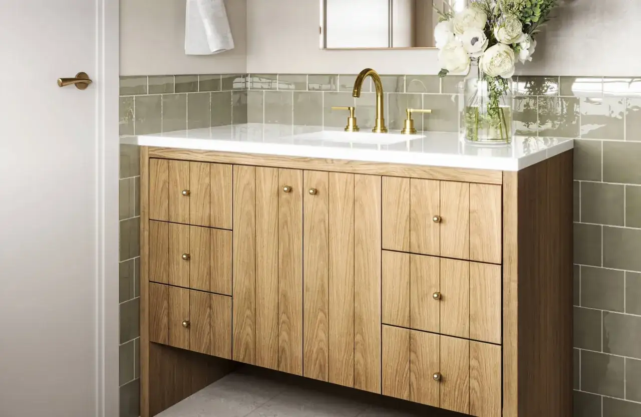 A modern bathroom vanity installation featuring a light wood cabinet with brass hardware, a white countertop, and a gold faucet.