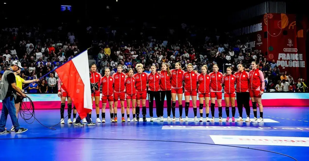 Piłka ręczna kadra Polski w czerwonych strojach, z flagą narodową, przed meczem z Francją.