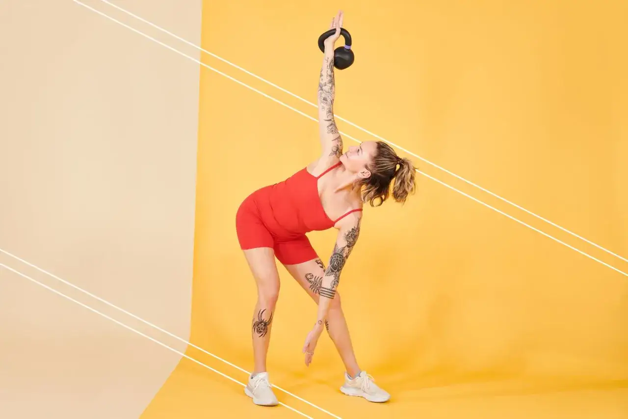 Kobieta wykonuje ćwiczenia z kettlebell, idealne dla początkujących. W tle ż&oacute;łta ściana.