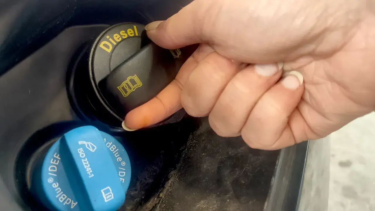 En hand skruvar på en svart dieselbehållare. Bredvid finns en blå AdBlue-behållare, viktig för att undvika problem med adblue fryspunkt.