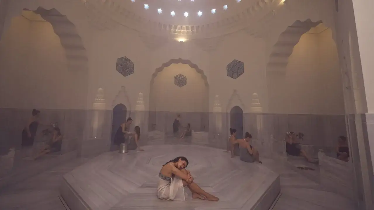 Frauen entspannen in einem dampfenden Hamam. Die Architektur und das Ambiente unterstreichen die tiefe **Hamam Bedeutung** von Reinigung und Erholung.