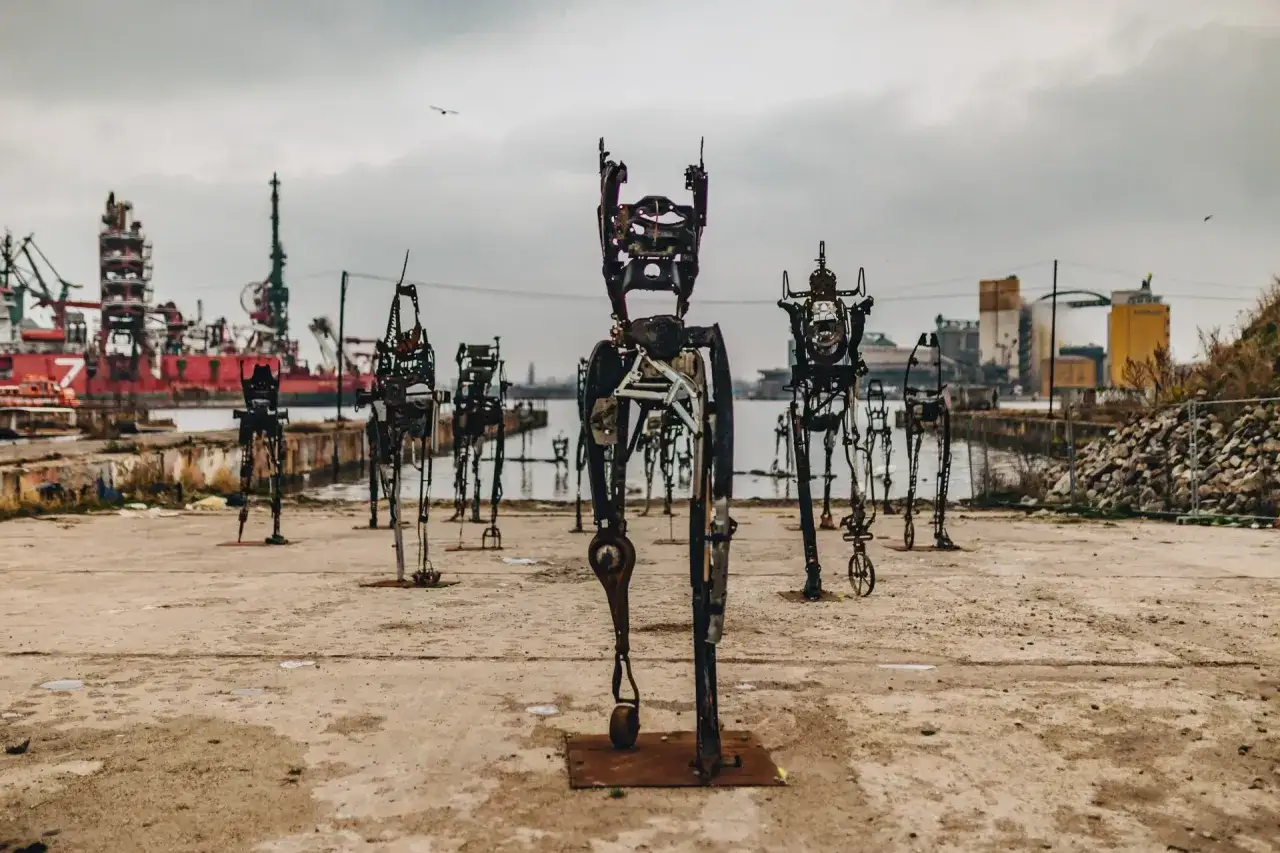Metalowe rzeźby ludzi na tle portu w Gdańsku. Nietypowe atrakcje Gdańsk czekają na odkrycie!