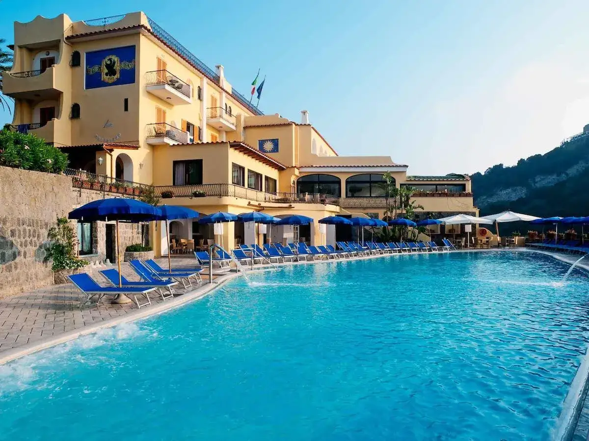 Piscina e lettini al **hotel terme tramonto d'oro Ischia**, con l'edificio giallo sullo sfondo e il cielo azzurro.