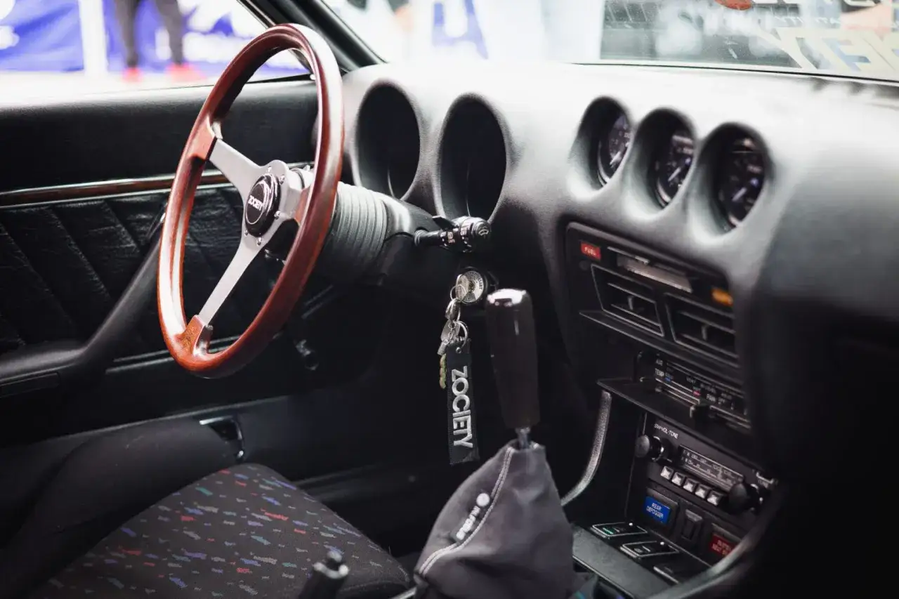 Wnętrze klasycznego Datsuna 280z z drewnianą kierownicą i sportową gałką zmiany biegów.