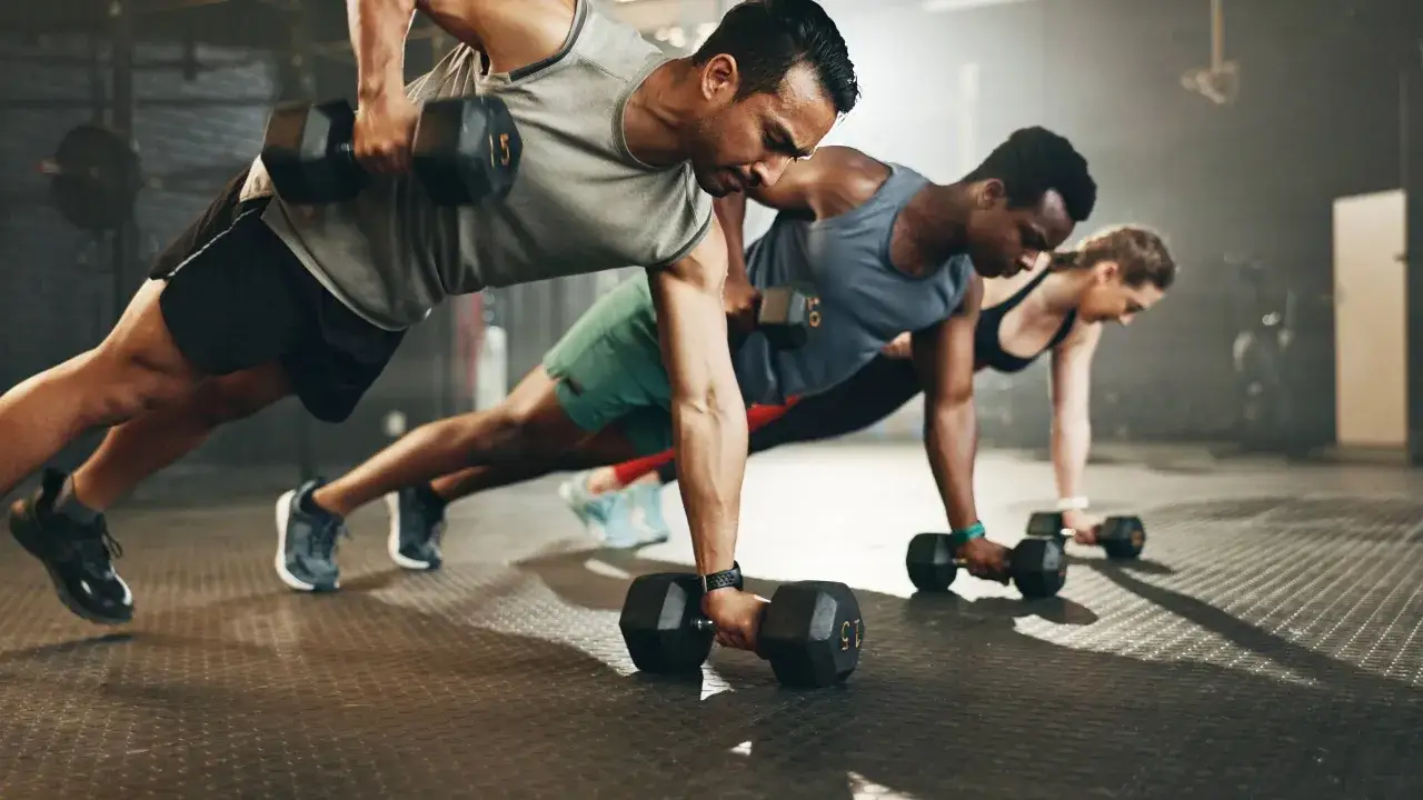 Drei Personen machen Liegestütze mit Hanteln. Sie fragen sich, wie viel Kalorien verbrennt man im Gym bei solchen Übungen.