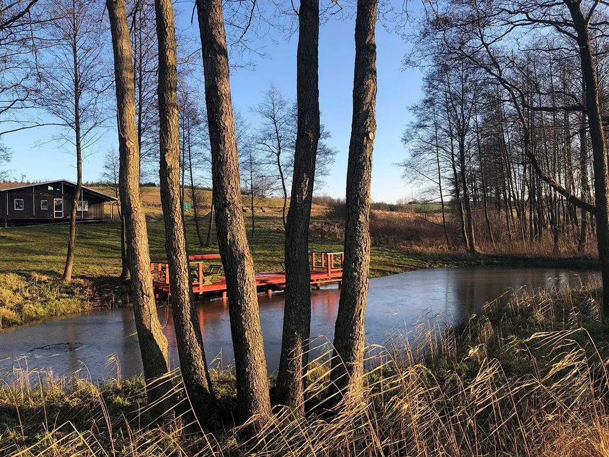 Zimowy dzień w miłej dolinie agroturystyka. Lodem pokryty staw, czerwony pomost i domek w tle.